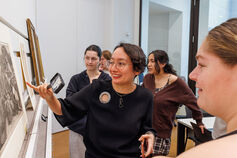 A female professor reviews a piece of artwork as students look on.